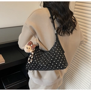 Close-up of black crossbody bag with white polka dots and a plush bear charm on a model