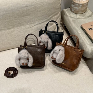 Three retro mini handbags in black and brown with cute plush rabbit charms on textile