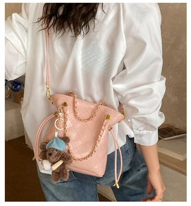Détail du sac seau matelassé rose avec chaîne dorée et breloque ours porté par le modèle
