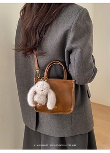 Close-up of retro brown faux leather handbag with golden handle and plush bunny charm