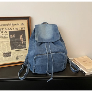 Detailed view of blue denim backpack with drawstring closure and front zip pocket