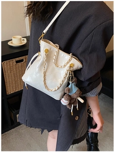 Détail du sac seau en cuir verni matelassé blanc avec chaîne dorée et breloque ours