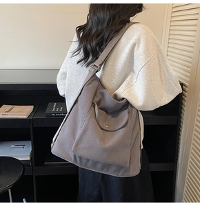 Detail of grey corduroy tote bag showing ribbed texture and metal buckle flap pocket on back
