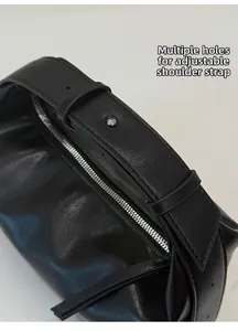 Detail of adjustable wide shoulder strap with silver metal buckles on black leather bag