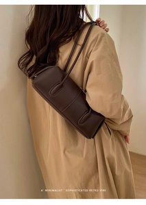 Detail of a vintage dark brown barrel bag worn by a model in a beige trench coat