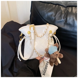 Détail du sac seau blanc matelassé avec chaîne dorée et breloque ours en peluche marron