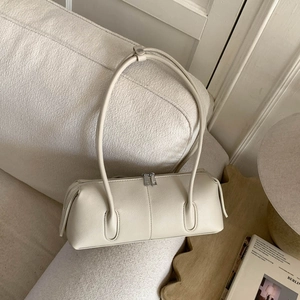 Minimalist beige barrel bag with leather texture placed on a stylish sofa set