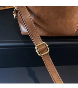 Detail of adjustable golden metal buckle and stitching on brown PU leather shoulder bag
