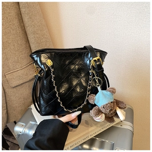 Détail d'un sac bandoulière noir matelassé avec chaîne dorée et breloque ours en peluche