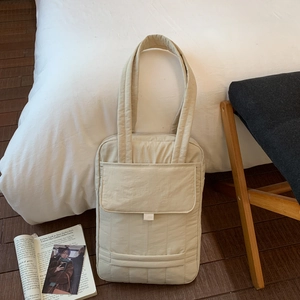 Macro detail of beige quilted nylon tote bag with front pocket in cozy bedroom setting