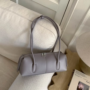 Detail view of a minimalist grey leather cylinder pillow bag with dual zippers on a white sofa