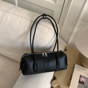 Detail of minimalist black Boston bag with double silver zippers on a soft fabric sofa