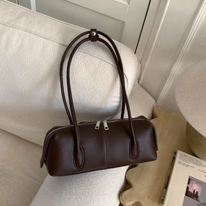 Detail of dark brown lychee leather pillow bag with silver zippers on a white sofa