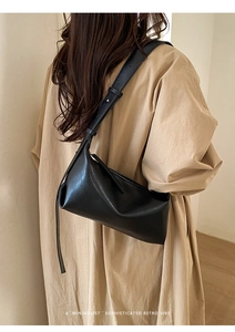 Black minimalist baguette bag with wide strap styled on a beige trench coat