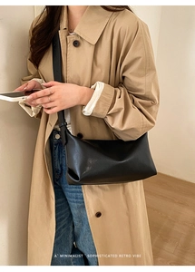 Close-up of minimalist black baguette bag with adjustable strap on a trench coat