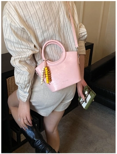 Detail of pink glossy leather bucket bag with unique handle and colorful beaded charm