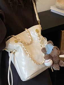 Sac seau matelassé beige avec bandoulière chaîne dorée et breloque ours en vue latérale