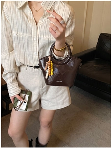 Close-up of deep brown patent leather bucket bag with glossy finish and beaded charm