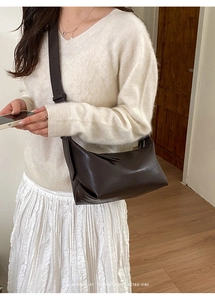 Minimalist dark brown baguette bag with wide strap worn over the shoulder by a model