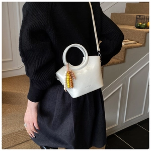 Close-up of white bucket bag with round handle and colorful bead charm on shoulder
