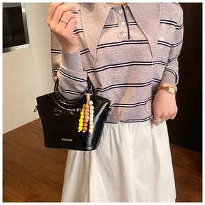 Detail of black glossy bucket bag with tricolor wooden beads on a striped knit sweater