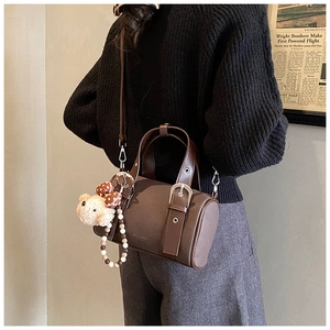 Detail view of dark brown bowling bag with bear charm and beaded strap on a model