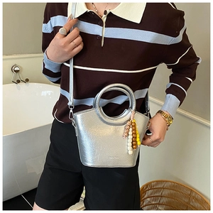 Silver metallic bucket bag with unique handle and colorful beaded charm on model