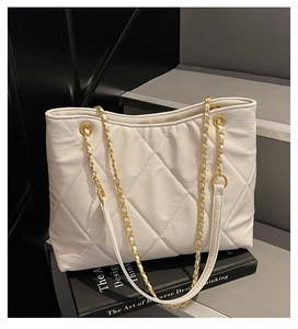 Detail of white quilted tote bag with golden metal eyelets and leather chain strap