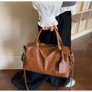 Close-up of brown Boston bag with vintage texture held by a model in a warm interior