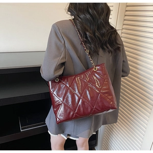 Detail of burgundy quilted tote bag with glossy finish and golden chain strap