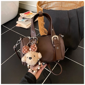 Detail view of dark brown leather bowling bag with silver buckles and plush puppy charm