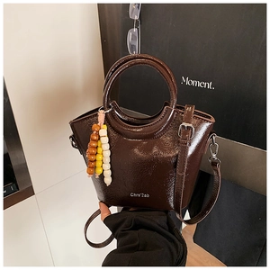 Detail of dark brown glossy bucket bag with circular handles and a beaded keychain