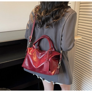 Deep red leather tote bag with round handles and adjustable shoulder strap on a model