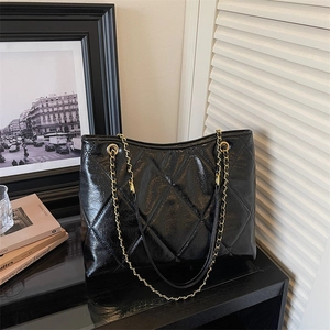 Détail du sac fourre-tout noir brillant matelassé avec chaîne dorée et bandoulière cuir