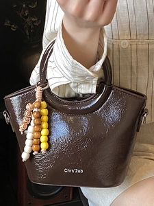 Dark brown patent leather bucket bag with white lettering and colorful beaded charm