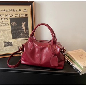 Macro detail of a burgundy wine leather Boston bag with dual handles on a vintage desk