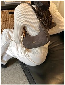 Detail of dark brown crescent bag with wood bead charm and metallic logo on the shoulder
