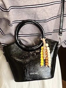 Chic black patent leather bucket bag with unique ring handle and colorful beaded charm