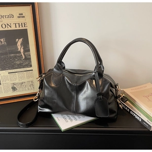 Close-up of black leather Boston handbag with gold hardware on a desk with vintage props