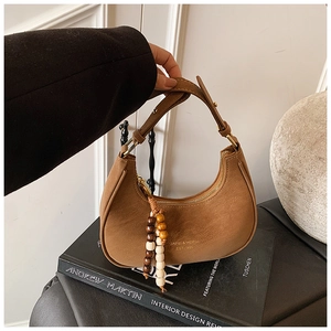 Detail of a brown leather crescent hobo bag featuring a beaded tassel and brand logo