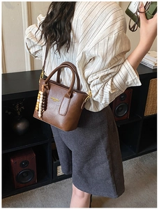Detail of a brown PU leather bucket bag with a wooden bead charm and fashion lettering