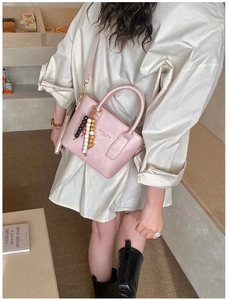 Detail of light pink leather handbag with bohemian tassel charm and gold logo lettering