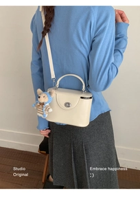 Off-white structured handbag featuring a cute teddy bear charm and sleek twist-lock closure