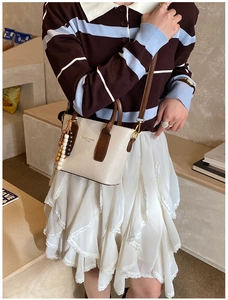 Detail of a cream and brown bucket bag with a beaded tassel on a striped dress