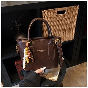 Close-up of brown textured bucket bag with retro round handle and beaded charm detail