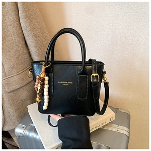 Detail of black leather Boston bag with beaded charm on a white book with suit background