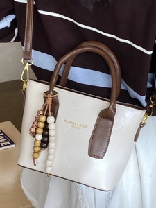 Fashionable beige leather bucket bag with brown handles and beaded charm for women