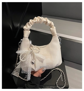 Detail of ruched handle and cream handbag with pearl bow and lace charm decoration