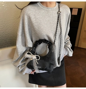 Close-up of black crossbody bag with pleated handle and white lace pearl bow charm