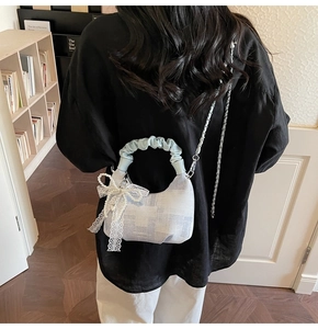 Detail of light blue plaid crossbody bag featuring a lace bow and pearl pendant